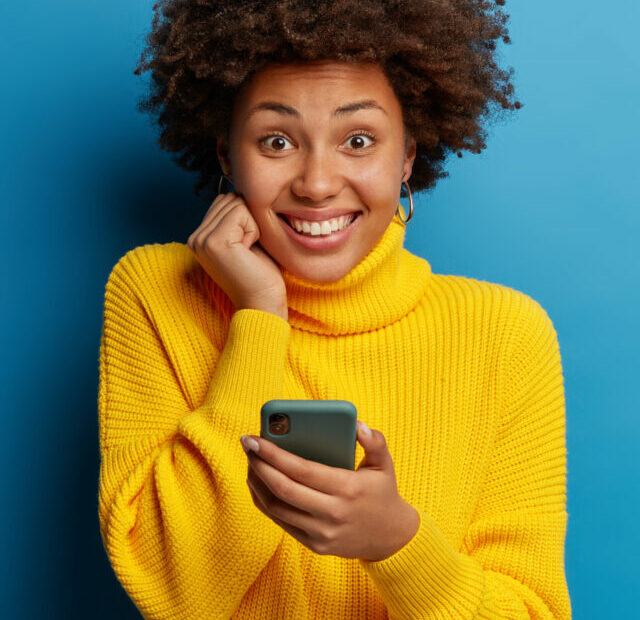 cropped-adorable-dark-skinned-adult-woman-dressed-yellow-jumper-using-mobile-phone-with-happy-expression.jpg