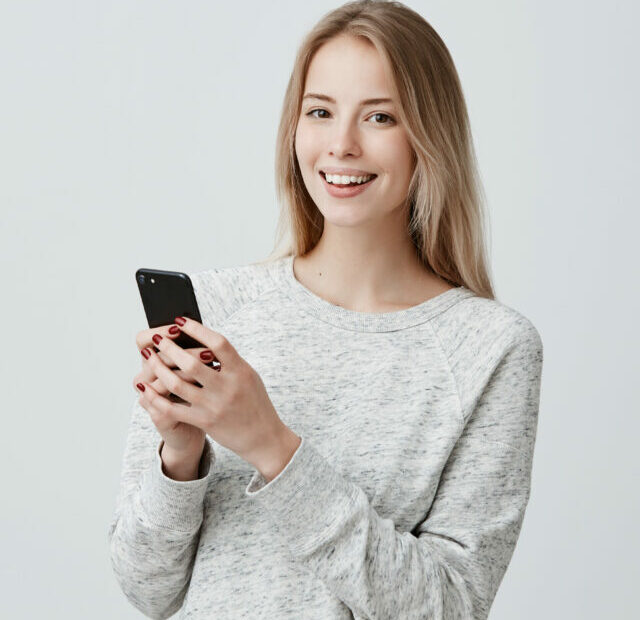 cropped-cheerful-young-blonde-haired-female-woman-with-cute-smile-posing-indoors-using-cell-phone-checking-newsfeed-her-social-network-accounts-pretty-woman-surfing-internet-mobile-1.jpg